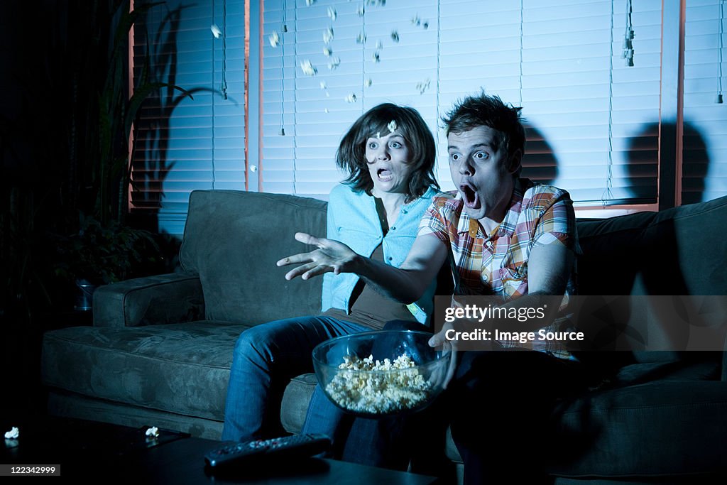 Young couple watching tv, man throwing popcorn