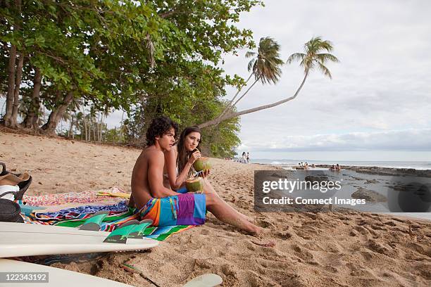 young couple sitting on beach drinking coconut milk - 2 coconut drinks ストックフォトと画像