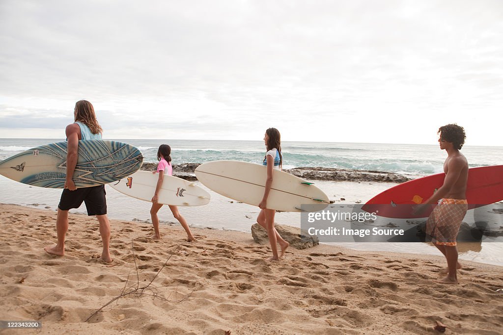 Four young friends carrying surfboards on beach