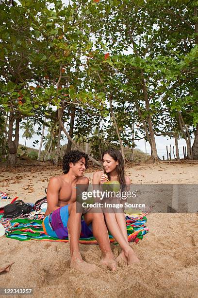 young couple sitting on beach drinking coconut milk - puerto rican woman stock pictures, royalty-free photos & images