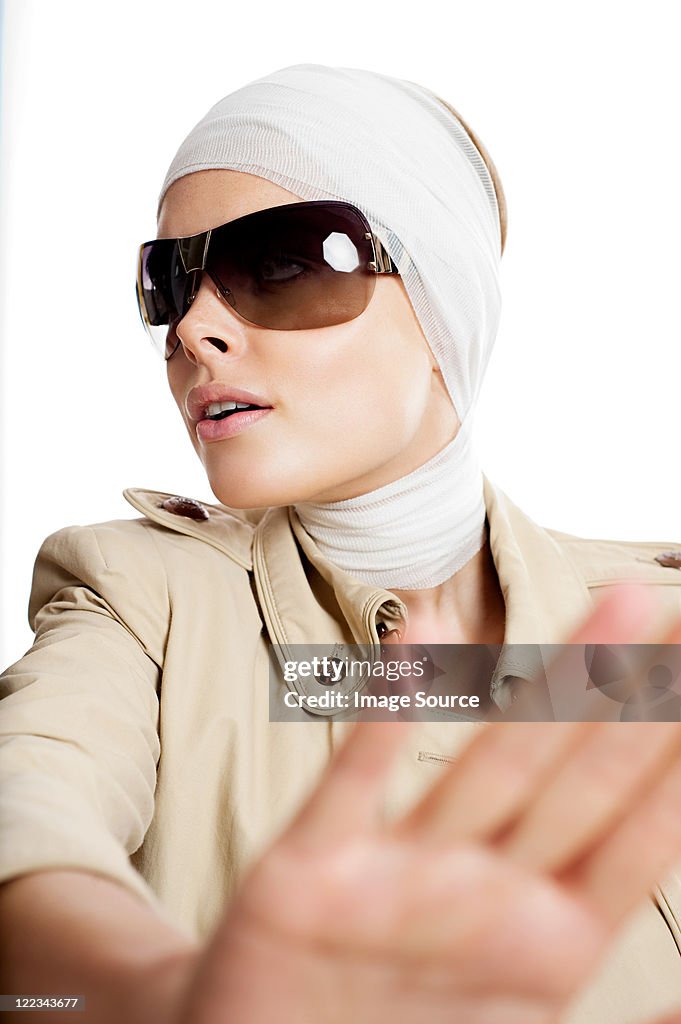 Young woman in sunglasses and bandages after cosmetic surgery