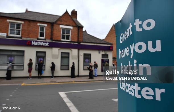 Customers socially distance as they queue to enter a NatWest bank, opposite a sign reading " Great to have you back in Leicester" in the North...