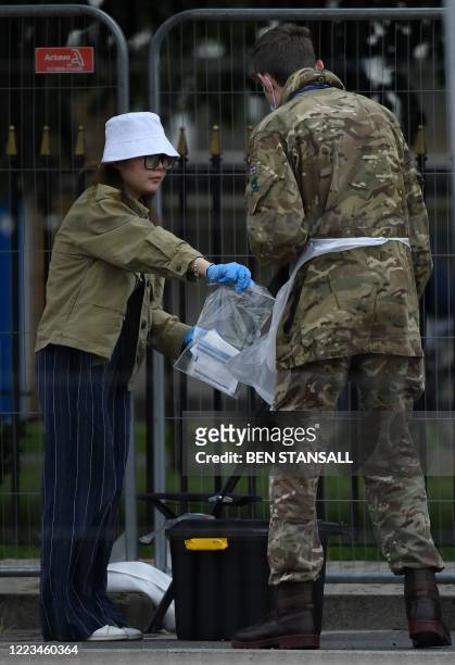 Member of the public puts a used self-test kit into a tub helped by a member of Britain's armed forces at a mobile COVID-19 testing centre, at...