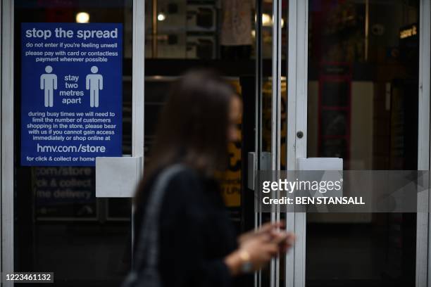 Pedestrian passes a sign on a shop window reminding customers to practice social distancing as a precaution against the spread of COVID-19 in the...