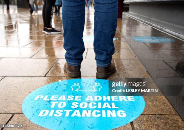 Shopper stands by a pavement sticker asking people to adhere to social distancing measures as they queue to enter a shop on Princes Street in...