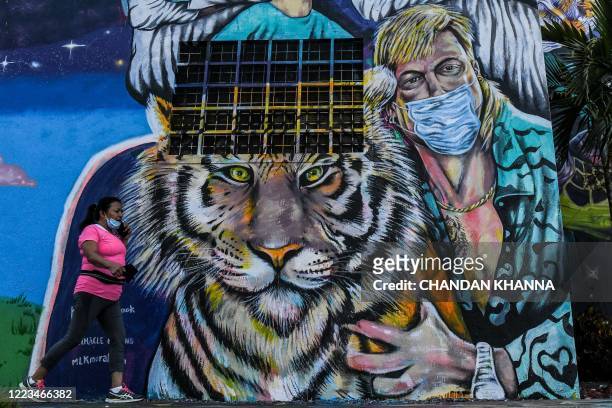 Woman walks past a mural by US muralist Kyle Holbrook with health workers and Joseph "Joe Exotic" Maldonado-Passage wearing a mask in Wynwood Art...