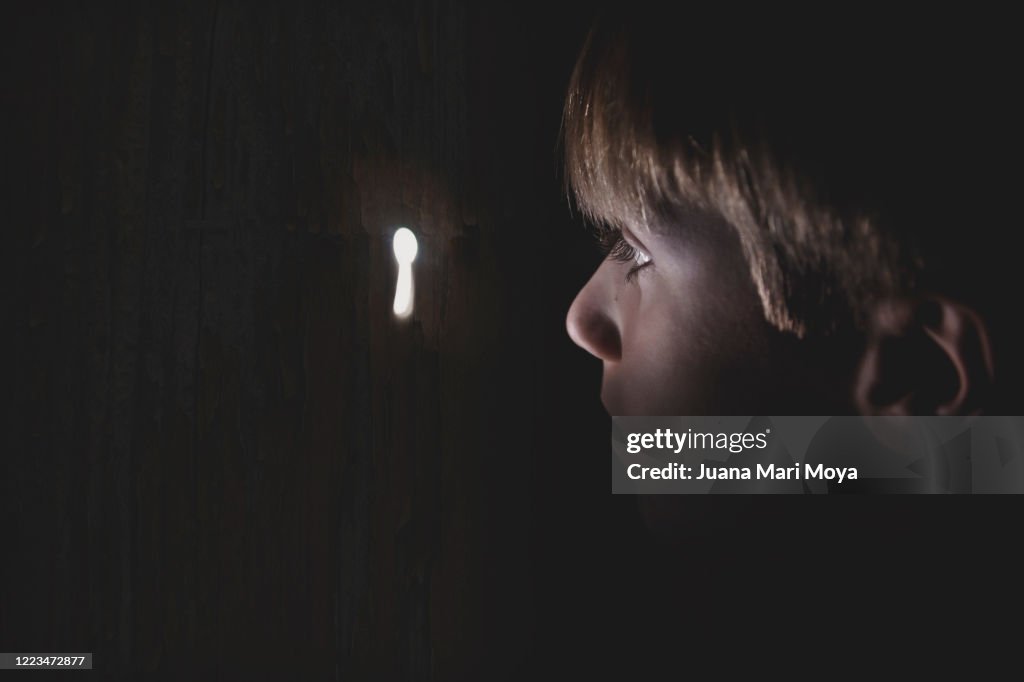 Close-up of a boy looking through a keyhole. Idyllic, fairy-tale-like image