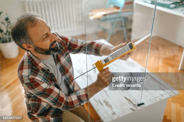man caulking a glass partition - cola material de escritório imagens e fotografias de stock