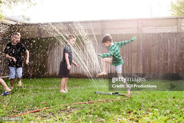 de jongens lopen en springen over sproeier op hete de zomerdag - water garden stockfoto's en -beelden