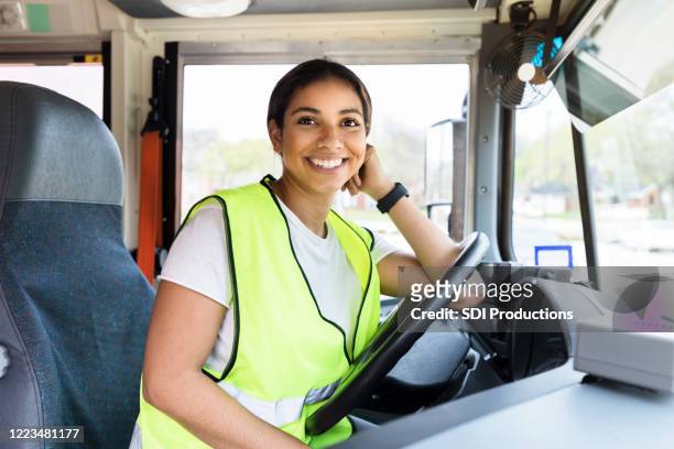 beautiful mid adult female bus driver leans on steering wheel - bus driver stock pictures, royalty-free photos & images