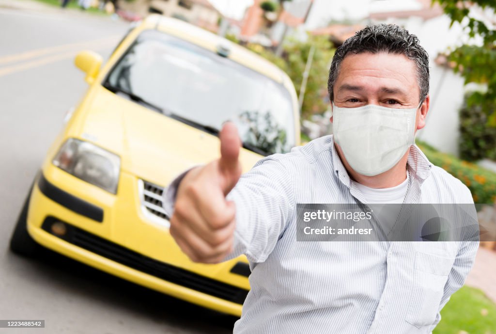 De bestuurder van de taxi met duimen omhoog en het dragen van een facemask