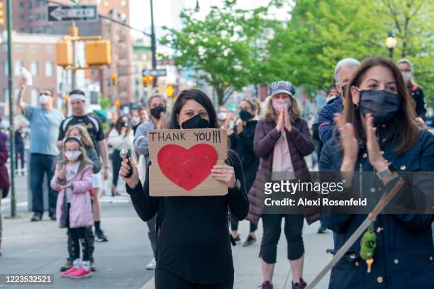Woman wearing a mask rings a bell and holds up a 'Thank You' sign outside of the Lenox Health Greenwich Village hospital during the nightly 'Clap...