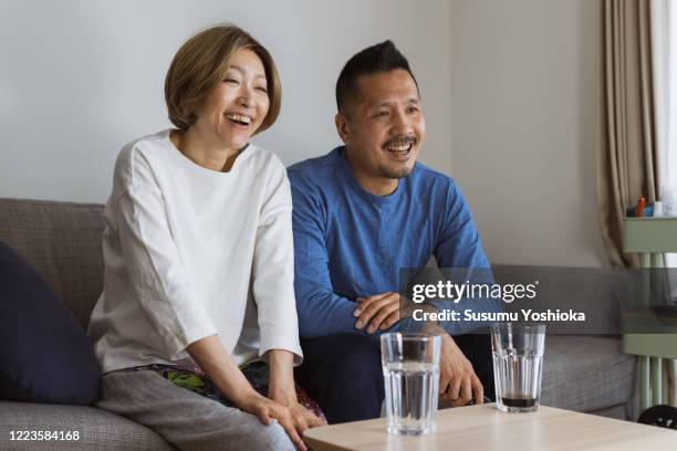 couple watching tv on sofa - pareja de mediana edad fotografías e imágenes de stock