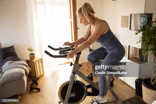 woman training on exercise bike at home - exercise bike stock pictures, royalty-free photos & images