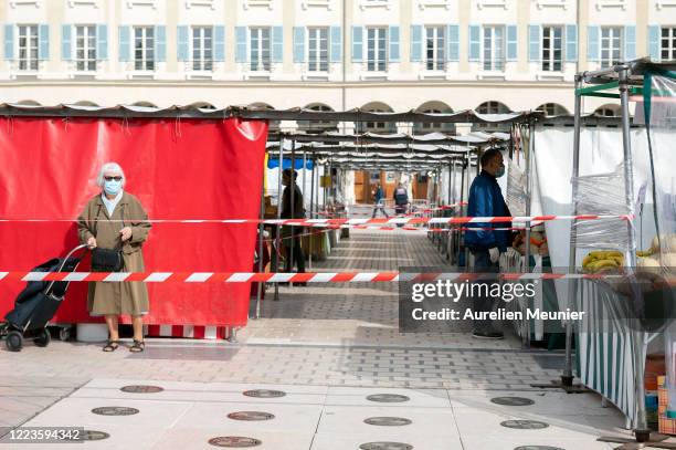 Woman wearing a face mask and pushing a trolley cart walks by market stalls protected by plastic films at an open-air market during the Coronavirus...