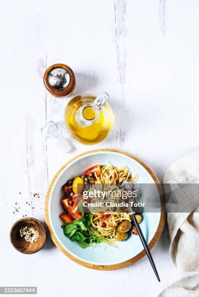 bowl of spaghetti with basil, tomatoes and olives on white, wooden background - service à condiments photos et images de collection