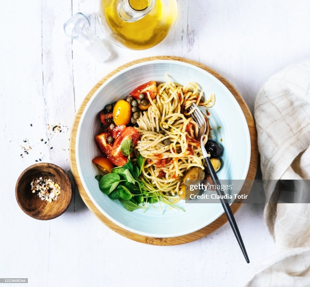 Bowl of spaghetti with basil, tomatoes and olives on white, wooden background