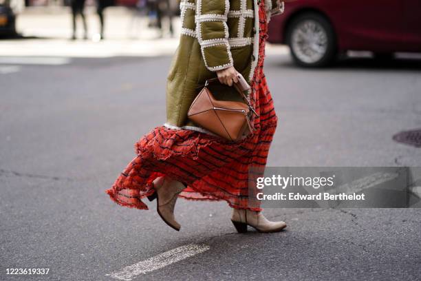 Guest wears a green khaki leather coat, a brown leather Loewe geometric shaped bag, a red and black striped mesh frilly dress, pointy boots, outside...