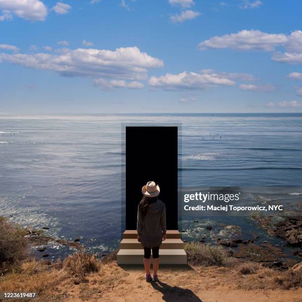 view of a young woman on the beach facing a door open in the landscape. - negative photo illusion stock pictures, royalty-free photos & images