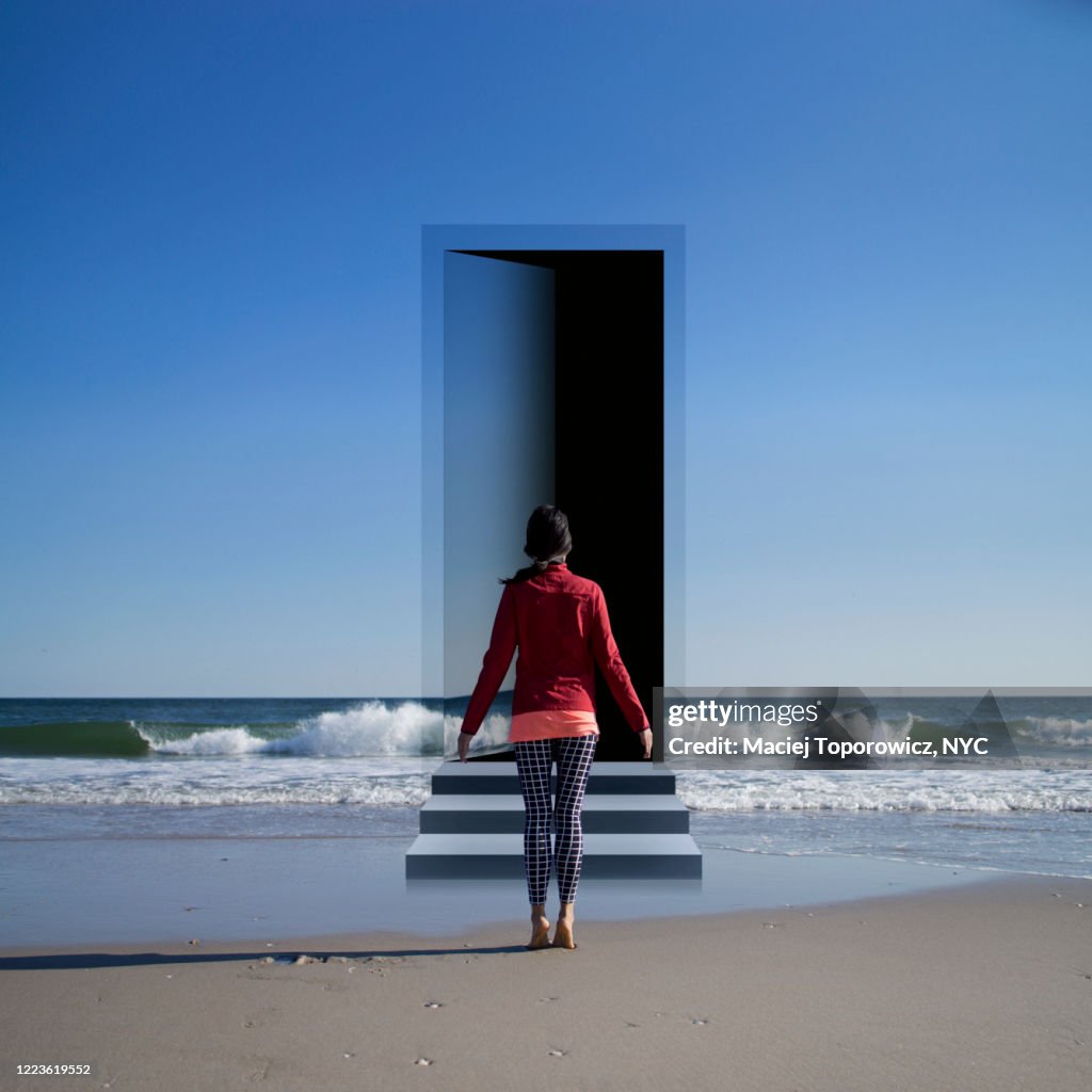 View of a young woman on the beach facing a door open in the landscape.