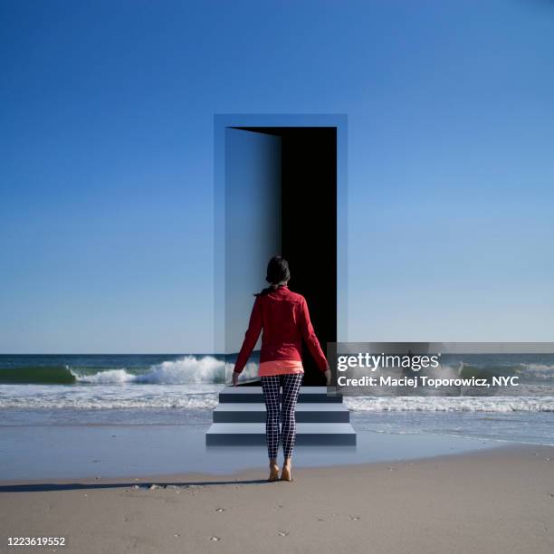 view of a young woman on the beach facing a door open in the landscape. - fantasy door stock pictures, royalty-free photos & images