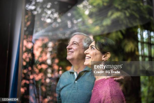 senior couple looking through window - anticipation stock pictures, royalty-free photos & images