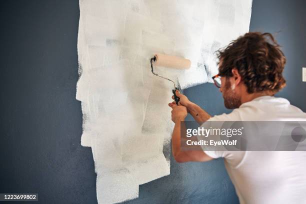 a man using two hands to paint a wall in his house with a paint roller. - diy top view stock pictures, royalty-free photos & images