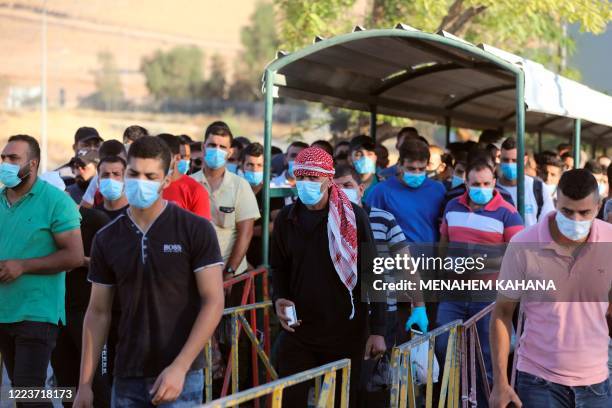 Palestinian workers wearing masks against Covid-19 lineup for a security check at the entrance to Israel's Mishor Adumim industrial zone nearby the...