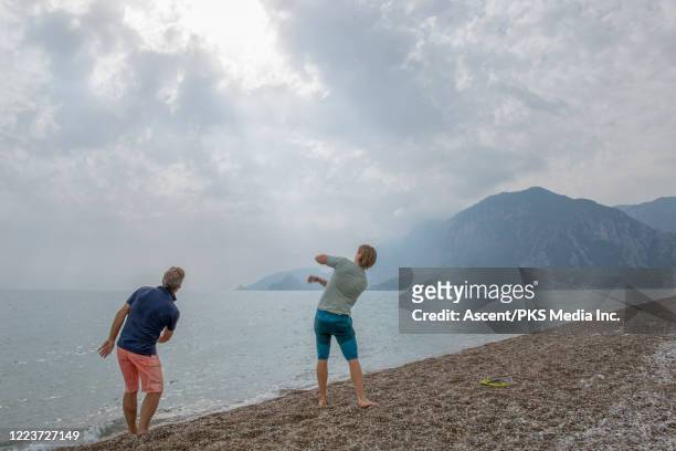 adult son and father skip stones across a calm sea - skimming stones stock pictures, royalty-free photos & images