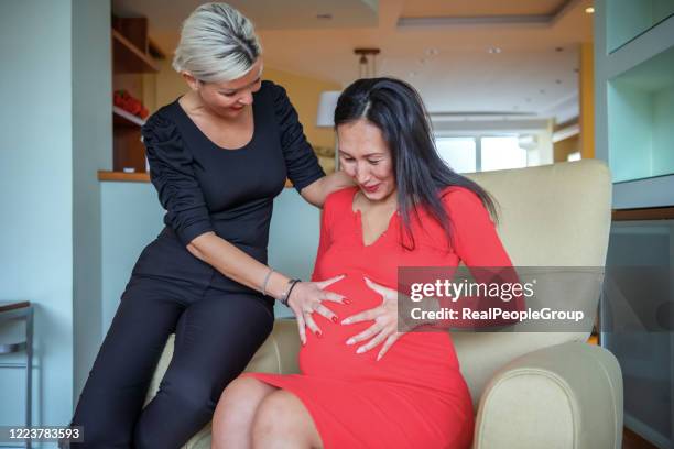 baby girl is moving in mamas stomach. beautiful woman is enjoying the pregnancy of her girlfriend - surrogacy stock pictures, royalty-free photos & images