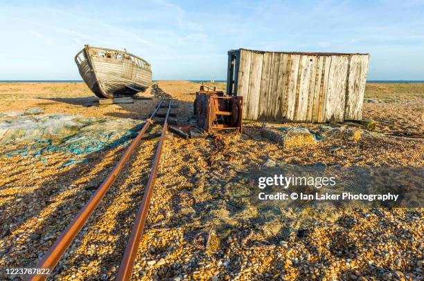 dungeness, kent, england, united kingdom. 24 january 2015. wrecked old fishing boat, winch gear and hut on dungeness beach. - dungeness stockfoto's en -beelden