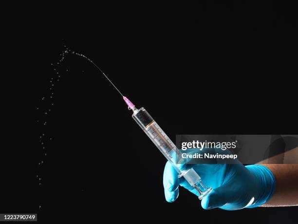 hands in blue gloves squirting a syringe on black background - squirting foto e immagini stock