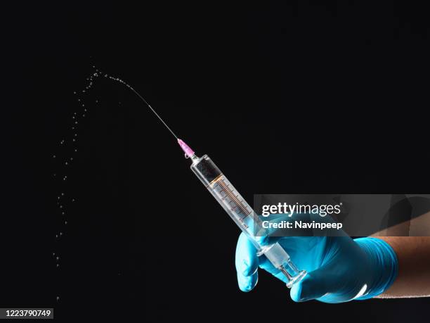 hands in blue gloves squirting a syringe on black background - squirting stock pictures, royalty-free photos & images