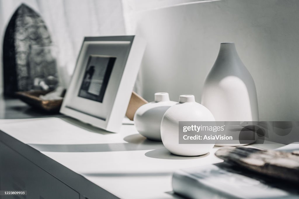 日光の窓のそばのキャビネットの中立色の花瓶と額縁の家の装飾