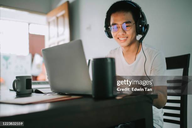 an asian chinese teenager chatting online with all his classmates via online software while doing his homework at the kitchen dining table together with his virtual assistant smart speaker - speech recognition stock pictures, royalty-free photos & images