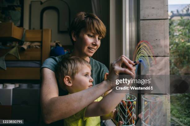 mother and little son drawing rainbow on window at home - family drawing stock pictures, royalty-free photos & images