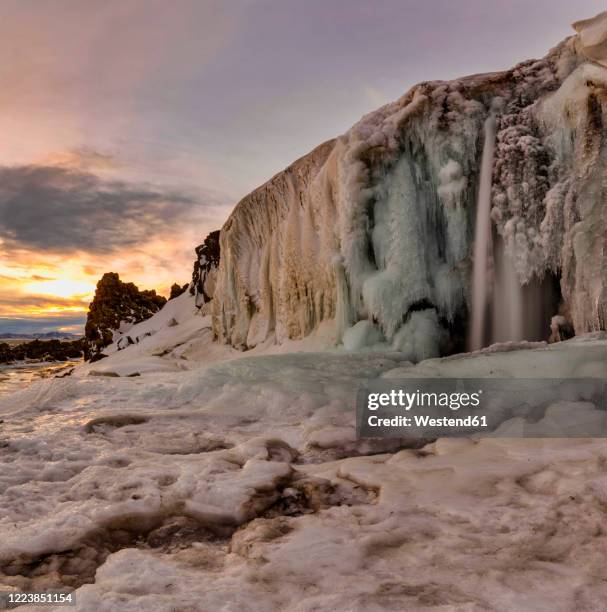 iceland, waterfall surrounded by icy landscape at sunset - frozen waterfall stock pictures, royalty-free photos & images