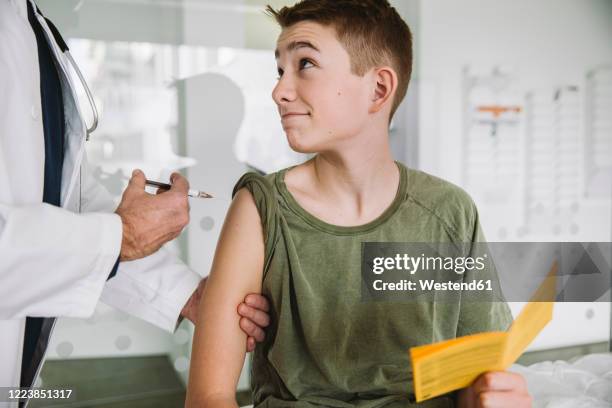 doctor injecting a vaccine into teenager?s arm - krankheitsverhinderung stock-fotos und bilder