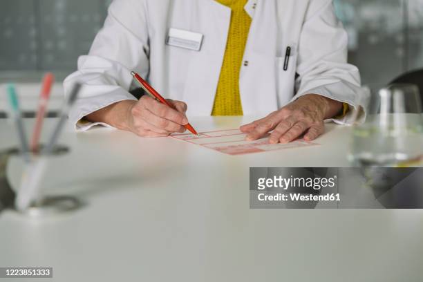 doctor sitting at desk filling out prescription - 50s woman writing at table imagens e fotografias de stock