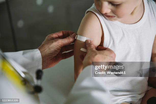 pediatrist putting band-aid onto arm of toddler after vaccination - bandage stockfoto's en -beelden