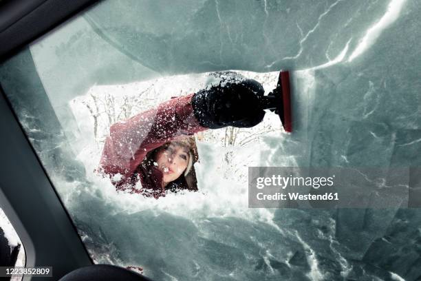 portrait of young woman cleaning snow from car's windscreen - eiskratzer stock-fotos und bilder