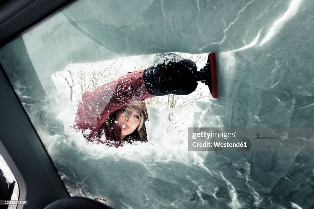Portrait of young woman cleaning snow from car's windscreen