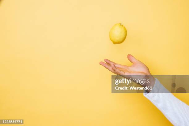 studio shot of hand of person tossing up lemon - throwing foto e immagini stock