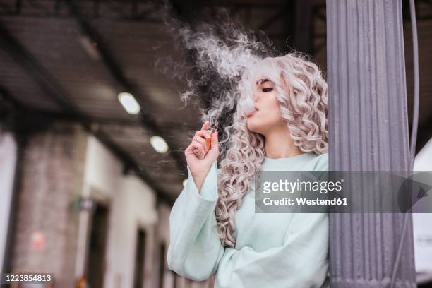 young woman smoking electronic cigarette on platform - vape stock-fotos und bilder