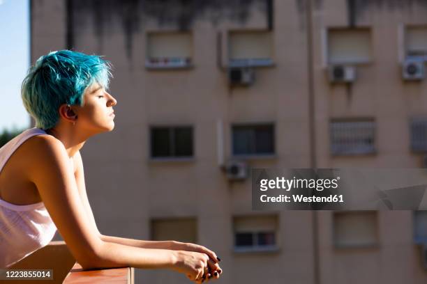 androgyne young woman with blue hair enjoying sunlight on balcony - androgynous stock pictures, royalty-free photos & images
