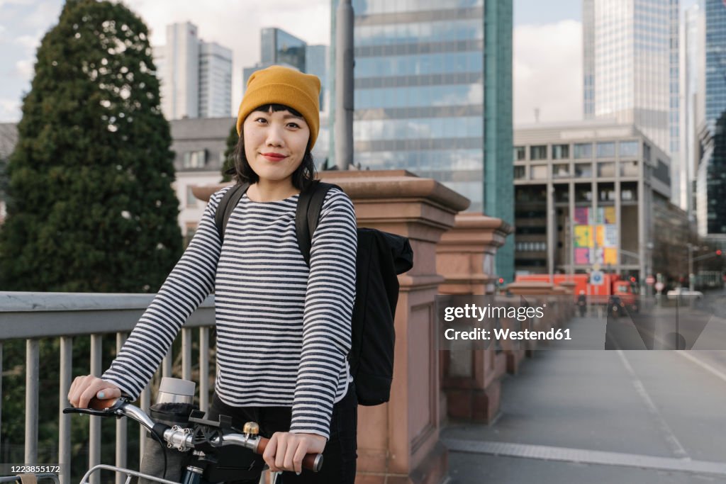 Portrait of confident woman with bicycle in the city, Frankfurt, Germany