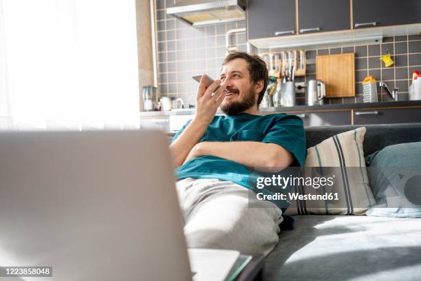 portrait of smiling man sitting on couch at home using mobile phone - jogging pants 個照片及圖片檔