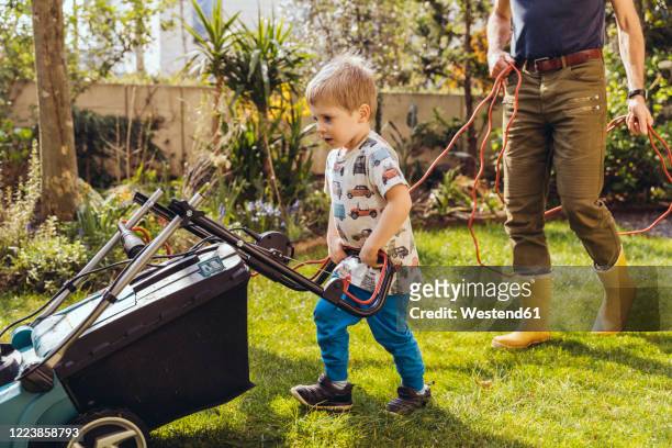 toddler boy mowing the lawn with his father - lawnmowing stock pictures, royalty-free photos & images