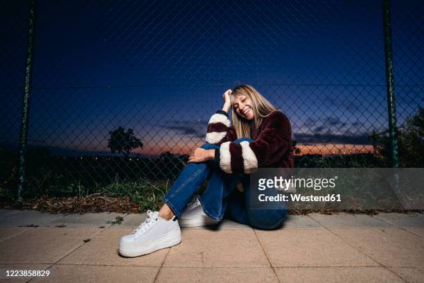 young woman wearing fur jacket, sitting on the ground at night - platform shoe stock pictures, royalty-free photos & images