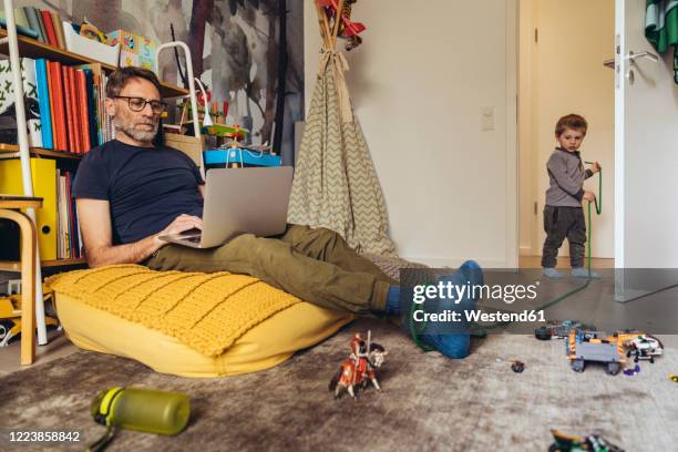 son tying his father working on laptop in children's room - working from home funny stock pictures, royalty-free photos & images